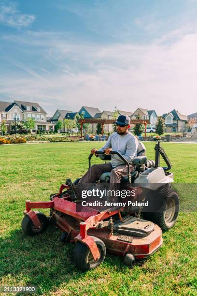 wide angle view of a latino man using a riding lawnmower to cut grass near an apartment complex with copy space - cortar relva imagens e fotografias de stock