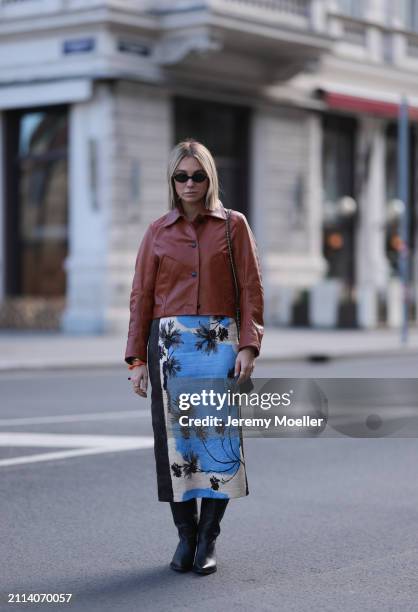 Karin Teigl seen wearing Miu Miu black oval sunglasses, Zara brown short leather jacket, Zara blue / white / black print pattern midi long skirt,...