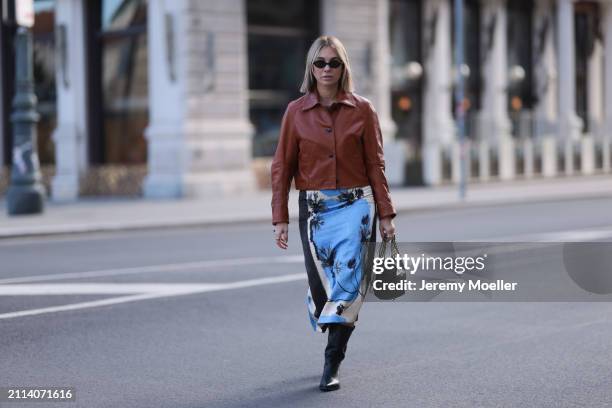 Karin Teigl seen wearing Miu Miu black oval sunglasses, Zara brown short leather jacket, Zara blue / white / black print pattern midi long skirt,...