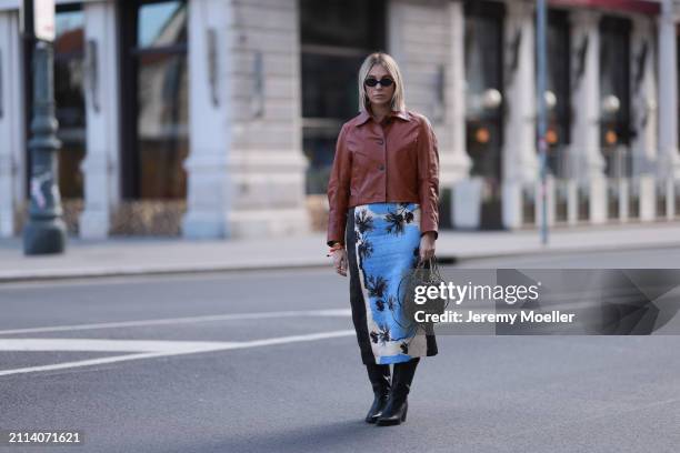 Karin Teigl seen wearing Miu Miu black oval sunglasses, Zara brown short leather jacket, Zara blue / white / black print pattern midi long skirt,...