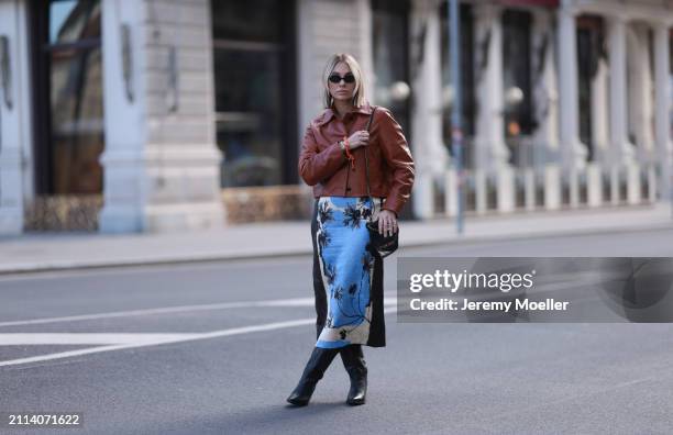 Karin Teigl seen wearing Miu Miu black oval sunglasses, Zara brown short leather jacket, Zara blue / white / black print pattern midi long skirt,...