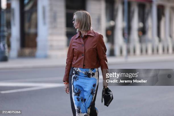 Karin Teigl seen wearing Miu Miu black oval sunglasses, Zara brown short leather jacket, Zara blue / white / black print pattern midi long skirt,...