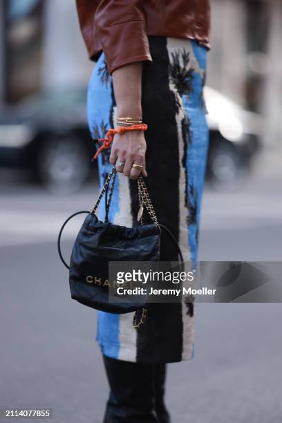 Karin Teigl seen wearing Zara brown leather short jacket, Zara blue / white / black print pattern midi long skirt, Chanel black leather 22 mini bag,...