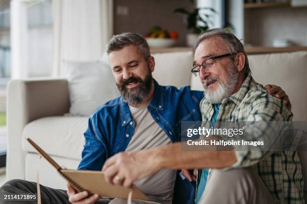 father and son looking at old photos in photo album, reminiscing about the son's childhood and family, recalling the old days. - family time stock pictures, royalty-free photos & images