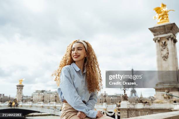 middle eastern curly gen z woman posing near pont alexandre iii in paris, france - eastern europe stockfoto's en -beelden