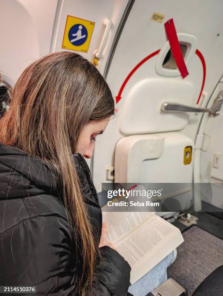 combining safety and comfort: a focused reader next to the illuminated emergency exit on an airplane - emergency exit stock pictures, royalty-free photos & images