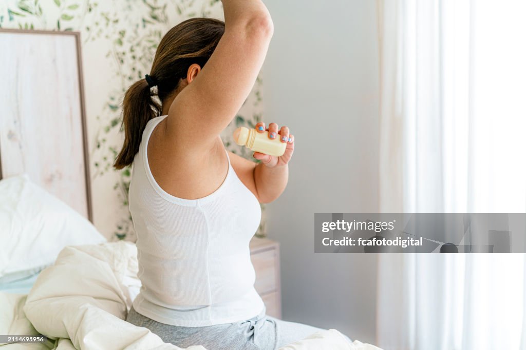 Woman applying antiperspirant roll underarms in the morning