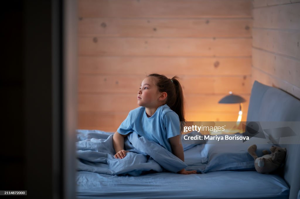 A girl in sky blue pajamas on a bed with blue linens with her toy rabbit. The ritual of putting children to bed.