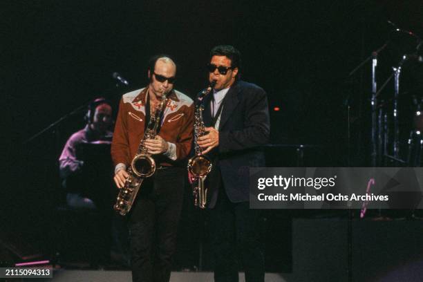 American comedian and actor Joe Piscopo, wearing sunglasses and holding a saxophone, alongside a second saxophonist on stage during 'The Joe Piscopo...