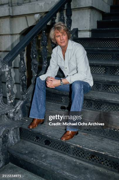American actor and singer Troy Donahue, wearing a light blue shirt, open at the collar, with jeans, sitting on the stoop of a property, United...