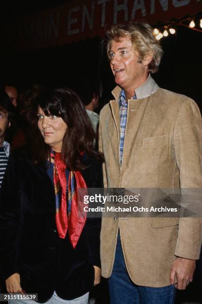 American actor and singer Troy Donahue, wearing a corduroy jacket with the collar raised jacket over a checked shirt, accompanied by a woman in a...