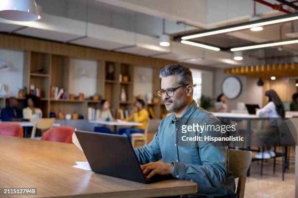 successful businessman working on his laptop at a coworking office - hispanolistic stock pictures, royalty-free photos & images