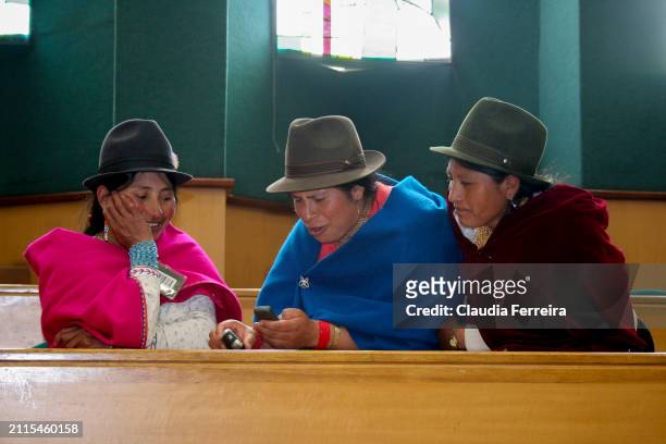 View of three people using a mobile phone as they attend the International Meeting of Indigenous Women and Ancestral Justice, Quito, Ecuador, between...