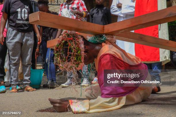 Boy dressed like Jesus lays down carrying a Cross during Good Friday commemoration in Kibera Slum on March 29, 2024 in Nairobi, Kenya.