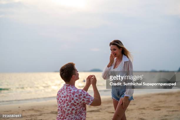 romantic beach wedding proposal: caucasian man surprises girlfriend with a sunset engagement by the ocean - chonburi province stock pictures, royalty-free photos & images