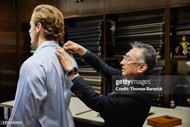 medium shot tailor measuring client for custom suit in workshop - tailor stock pictures, royalty-free photos & images