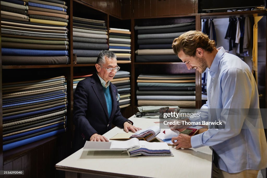 Medium wide shot client looking at fabric samples in tailors workshop