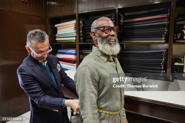 medium wide shot tailor measuring client for custom suit in workshop - schneiderberuf stock-fotos und bilder