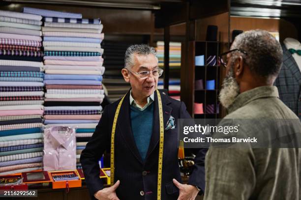 medium shot tailor in discussion with client ordering suit in workshop - tailor made suit stock pictures, royalty-free photos & images
