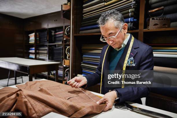medium shot tailor working on custom sportscoat at table in workshop - schneiderberuf stock-fotos und bilder