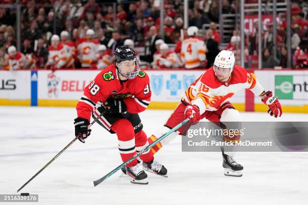 Connor Bedard of the Chicago Blackhawks skates with the puck against Nikita Okhotiuk of the Calgary Flames during the second period at the United...