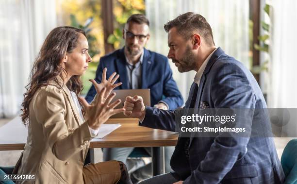 woman gesticulates to a man angry over disagreement with male mediator sitting behind the table in the background. - divorce photos et images de collection