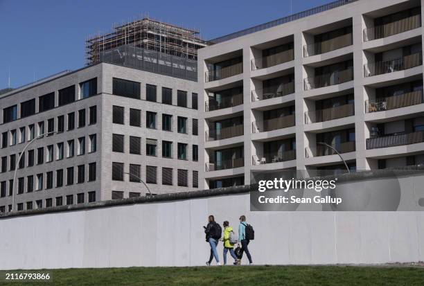 People walk past a surviving section of the Berlin Wall as a new residential apartment building tower stands under construction behind on March 27,...