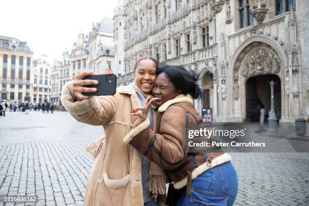 two young women taking a selfie outside brussels town hall - brussel stockfoto's en -beelden