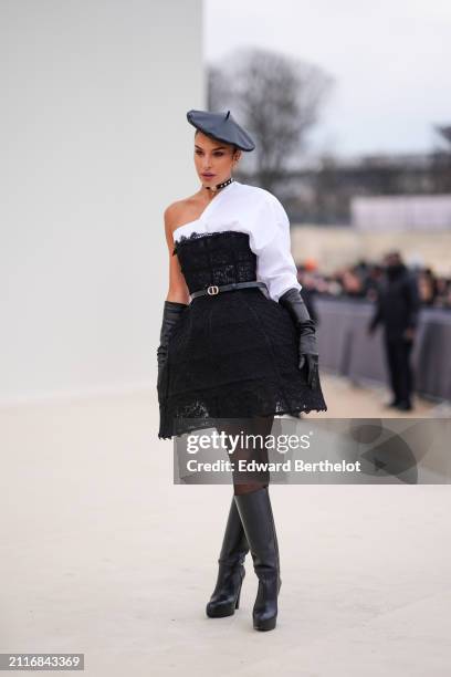 Jessica Aidi wears a black leather beret hat, a choker, a white asymmetric shirt, black elbow length leather gloves, a Dior leather thin belt, a...