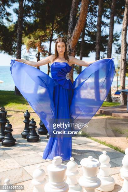beautiful young fashion model in long blue strapless dress, lifting train in the park at the seaside - strapless dress stock pictures, royalty-free photos & images