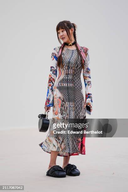 Guest wears a choker, a long dress with long sleeves with printed colored floral details and geometric patterns, a black leather heart-shaped bag,...