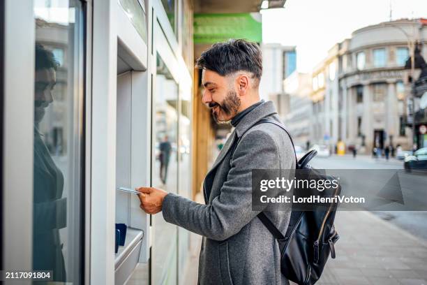 hombre usando un cajero automático en la ciudad - rótulo con el horario fotografías e imágenes de stock