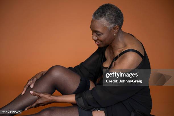 relaxed black woman putting on silk stockings - mb stock pictures, royalty-free photos & images