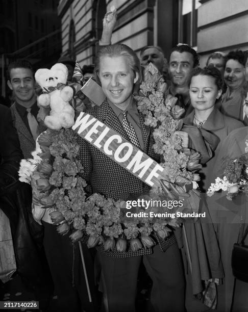 Russian clown Oleg Popov wears a wreath made of tulips, a 'Welcome' sign and a teddy bear while in London with the Moscow State Circus, May 26th 1956.