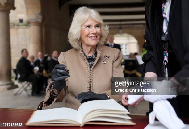 Queen Camilla smiles as she signs the visitors book at the Old Market Hall during her visit to the Farmers' Market on March 27, 2024 in Shrewsbury,...