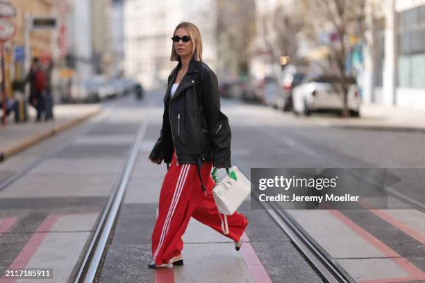 Karin Teigl seen wearing Miu Miu black oval sunglasses, gold necklaces, CYK white cotton basic top, Acne Studios black leather biker jacket, Adidas...