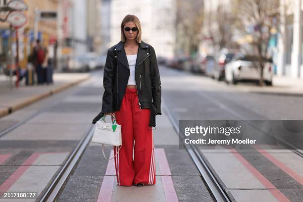 Karin Teigl seen wearing Miu Miu black oval sunglasses, gold necklaces, CYK white cotton basic top, Acne Studios black leather biker jacket, Adidas...