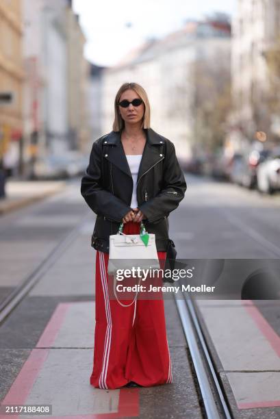 Karin Teigl seen wearing Miu Miu black oval sunglasses, gold necklaces, CYK white cotton basic top, Acne Studios black leather biker jacket, Adidas...