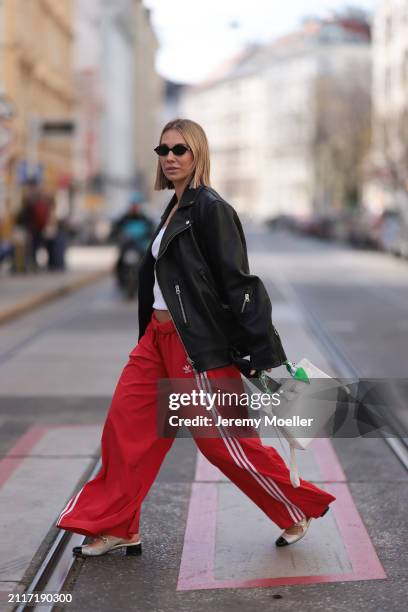 Karin Teigl seen wearing Miu Miu black oval sunglasses, gold necklaces, CYK white cotton basic top, Acne Studios black leather biker jacket, Adidas...