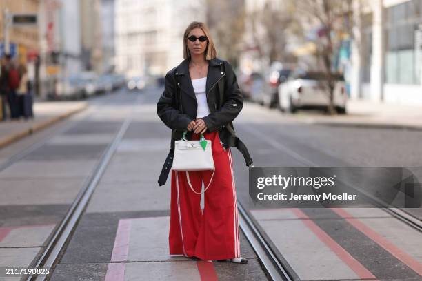 Karin Teigl seen wearing Miu Miu black oval sunglasses, gold necklaces, CYK white cotton basic top, Acne Studios black leather biker jacket, Adidas...