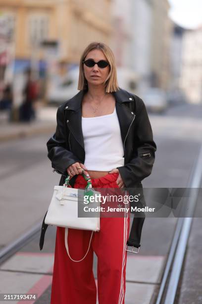 Karin Teigl seen wearing Miu Miu black oval sunglasses, gold necklaces, CYK white cotton basic top, Acne Studios black leather biker jacket, Adidas...