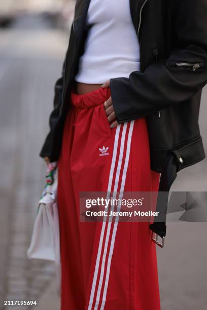 Karin Teigl seen wearing CYK white cotton basic top, Acne Studios black leather biker jacket, Adidas red long wide leg track pants, Hermès white...