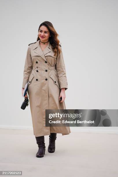Guest wears a beige trench long coat , black leather boots, outside Dior, during the Womenswear Fall/Winter 2024/2025 as part of Paris Fashion Week...