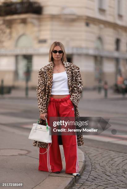 Karin Teigl seen wearing Miu Miu black oval sunglasses, gold necklaces, CYK white cotton basic top, H&M Studios leopard print pattern long coat,...