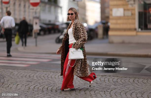 Karin Teigl seen wearing Miu Miu black oval sunglasses, gold necklaces, CYK white cotton basic top, H&M Studios leopard print pattern long coat,...