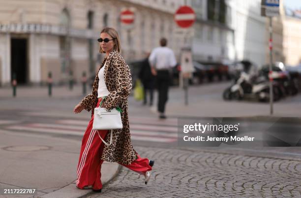 Karin Teigl seen wearing Miu Miu black oval sunglasses, gold necklaces, CYK white cotton basic top, H&M Studios leopard print pattern long coat,...