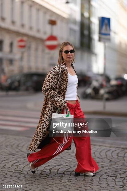 Karin Teigl seen wearing Miu Miu black oval sunglasses, gold necklaces, CYK white cotton basic top, H&M Studios leopard print pattern long coat,...