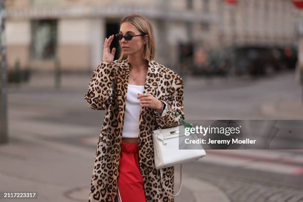 Karin Teigl seen wearing Miu Miu black oval sunglasses, gold necklaces, CYK white cotton basic top, H&M Studios leopard print pattern long coat,...