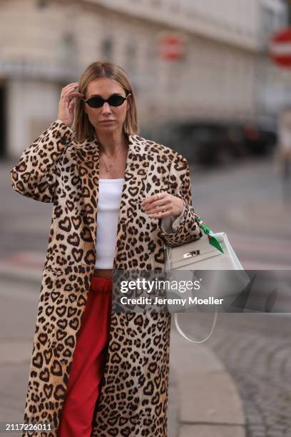 Karin Teigl seen wearing Miu Miu black oval sunglasses, gold necklaces, CYK white cotton basic top, H&M Studios leopard print pattern long coat,...