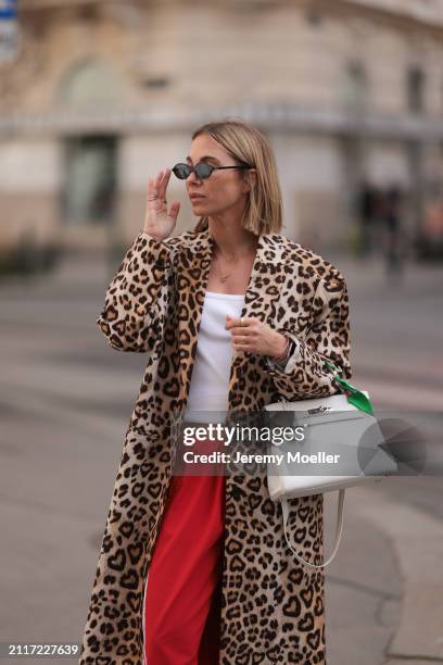 Karin Teigl seen wearing Miu Miu black oval sunglasses, gold necklaces, CYK white cotton basic top, H&M Studios leopard print pattern long coat,...